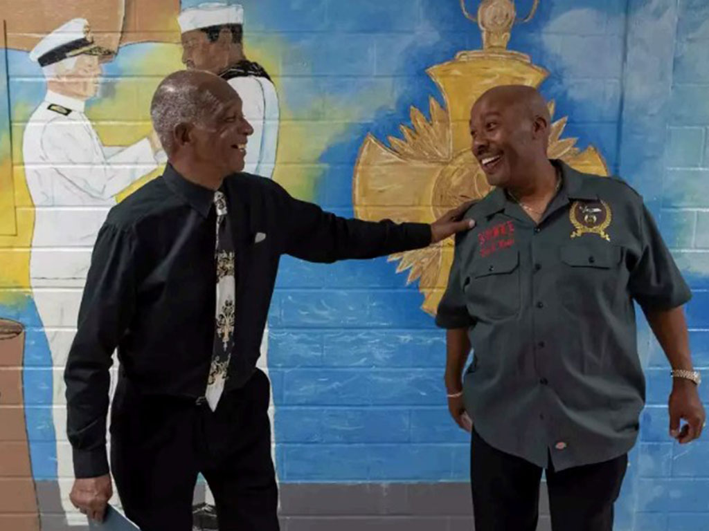 Two men greeting each other in front of a mural
