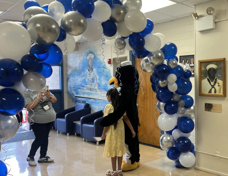 Student and mascot standing under balloon arch